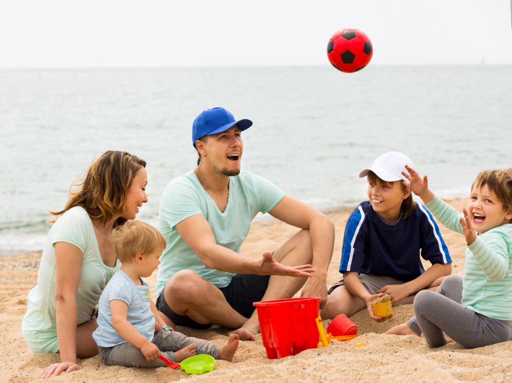 Happy family playing with ball at sandy beach